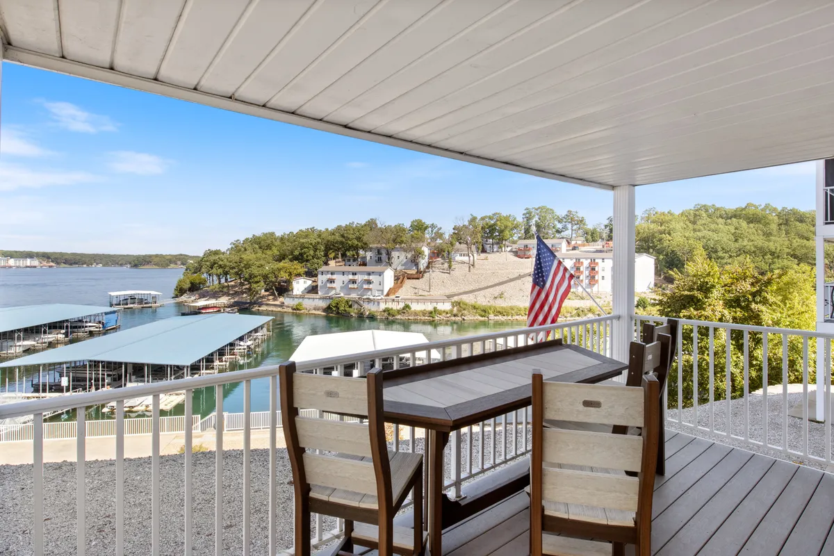 A spacious outdoor dining area overlooking the water, featuring a table set for gatherings, an American flag, and a scenic marina backdrop. The area is vibrant and inviting for socializing or relaxing.