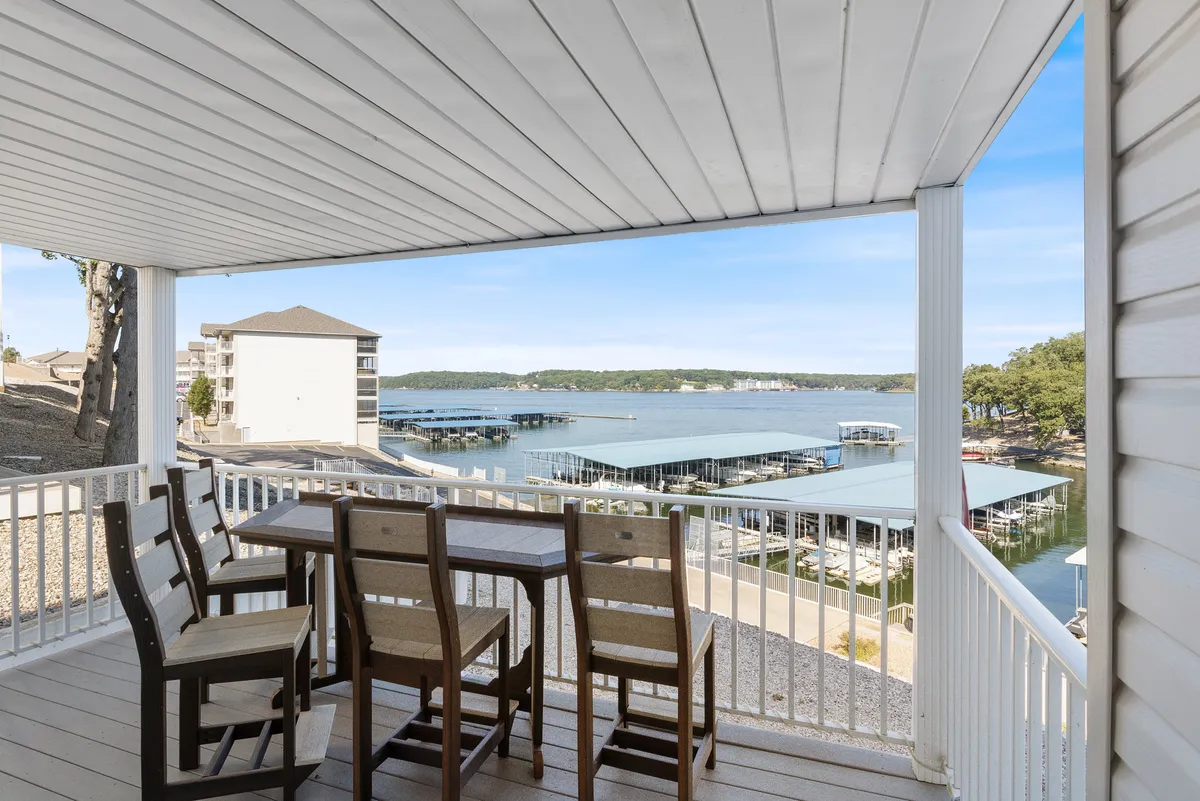 An outdoor dining table set on a patio with a clear waterfront view and a vibrant marina in the distance. The setting is tranquil yet social, inviting guests to enjoy al fresco meals, morning coffees, or sunset gatherings while soaking in the lakeside ambiance.