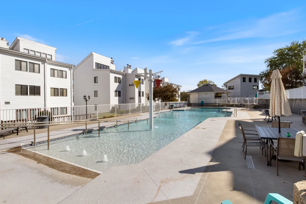 A vibrant outdoor swimming pool surrounded by comfortable seating, lush landscaping, and sparkling water features. The area is spacious and designed for both relaxation and play, with shaded spots and plenty of room for families to gather.
