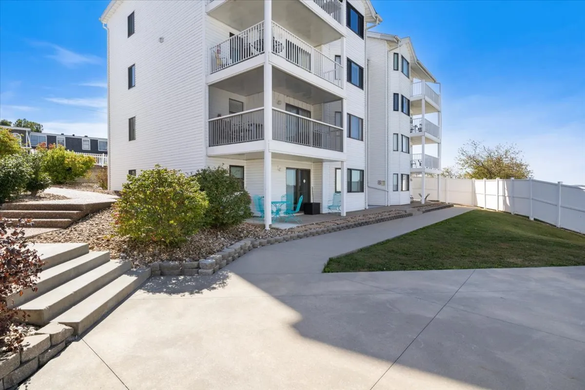 A welcoming exterior setting featuring balconies, green shrubs, and a winding pathway. The balconies invite cozy mornings or evenings with coffee or a glass of wine, while the landscaped path connects the condo to the greater community and waterfront.