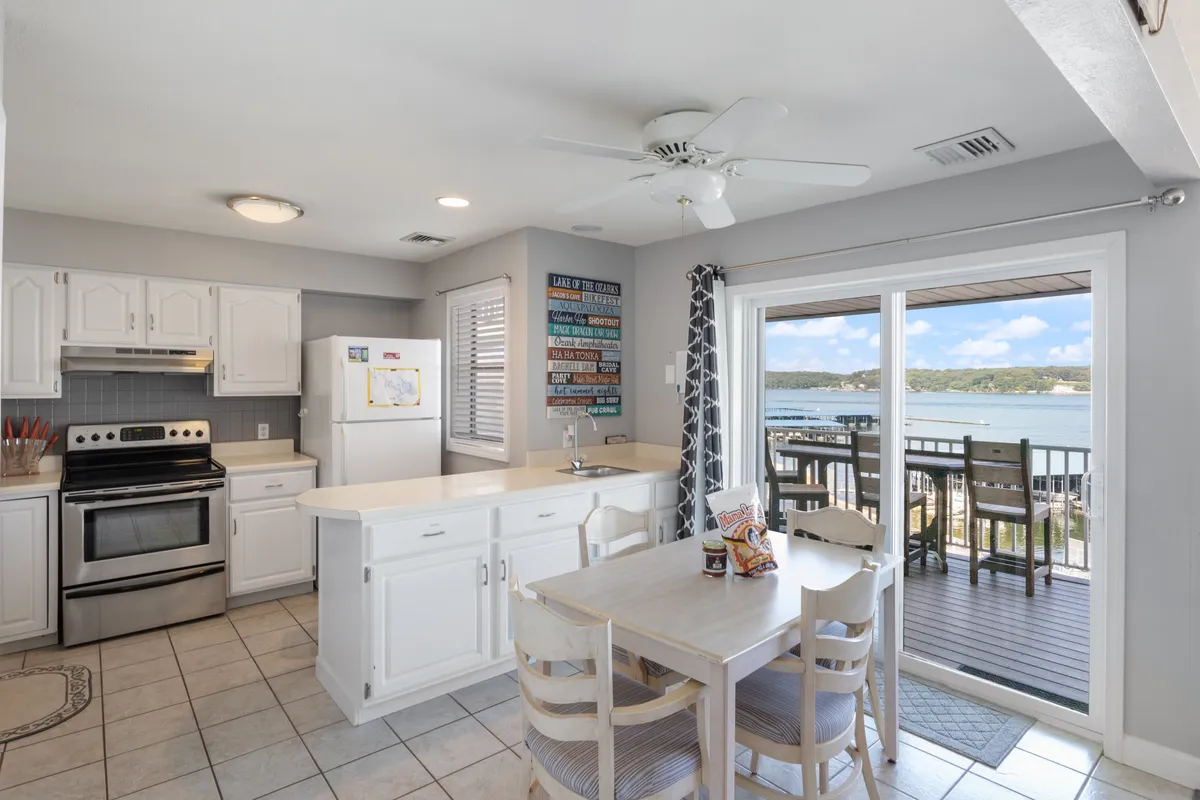 This image captures the open-concept kitchen with a kitchen island and a dining table, both of which are key focal points for meal preparation and gathering. A sliding glass door brings in natural light and offers a view of the lake, visually connecting the kitchen and dining area to the scenic outdoors.
