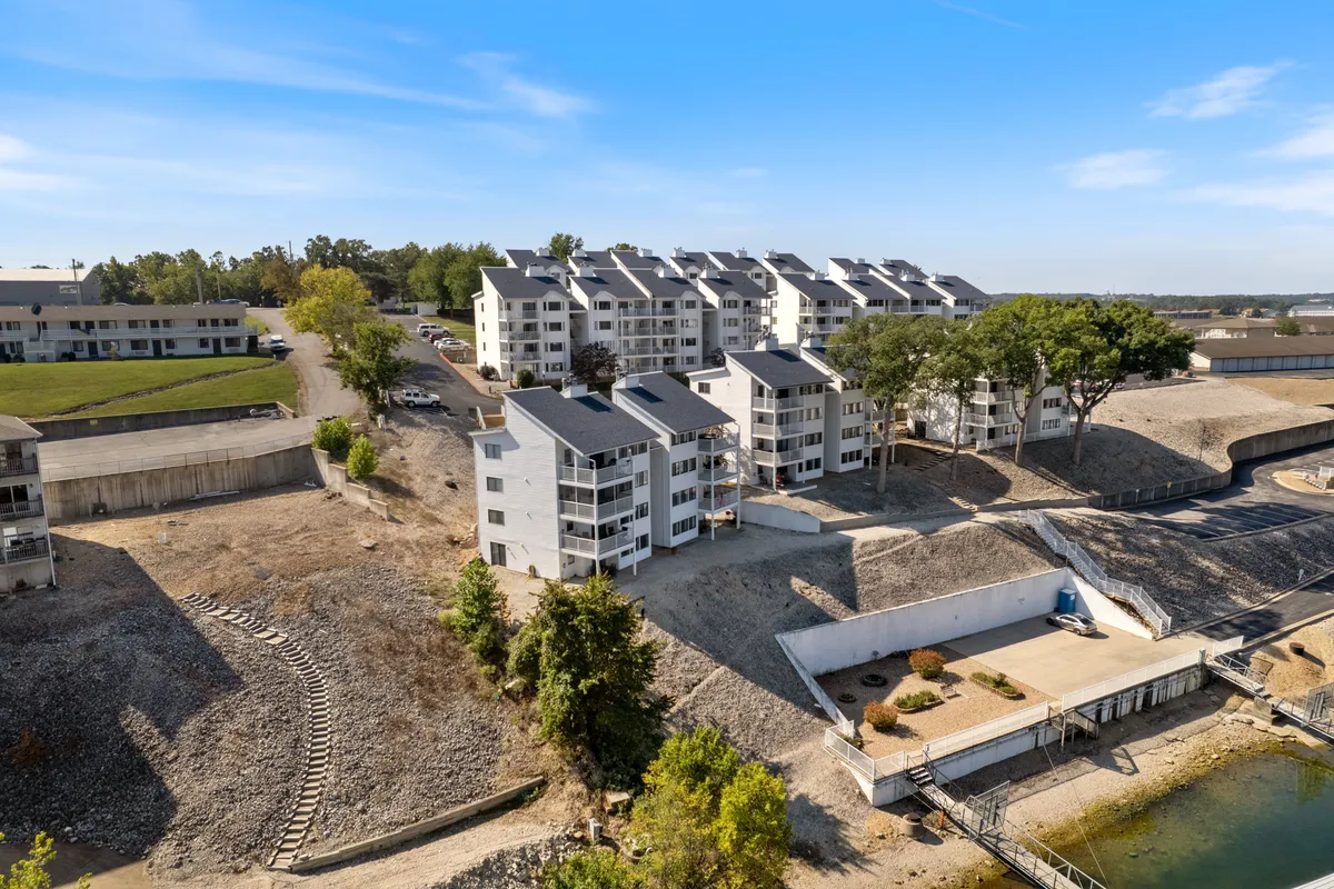 A contemporary multi-unit building sits beside a lush, green lakefront area. The shoreline is visible, with open space for walks, picnics, or simply enjoying the sunset. The setting exudes relaxation and privacy, emphasizing the retreat’s proximity to natural beauty and lakeside attractions.
