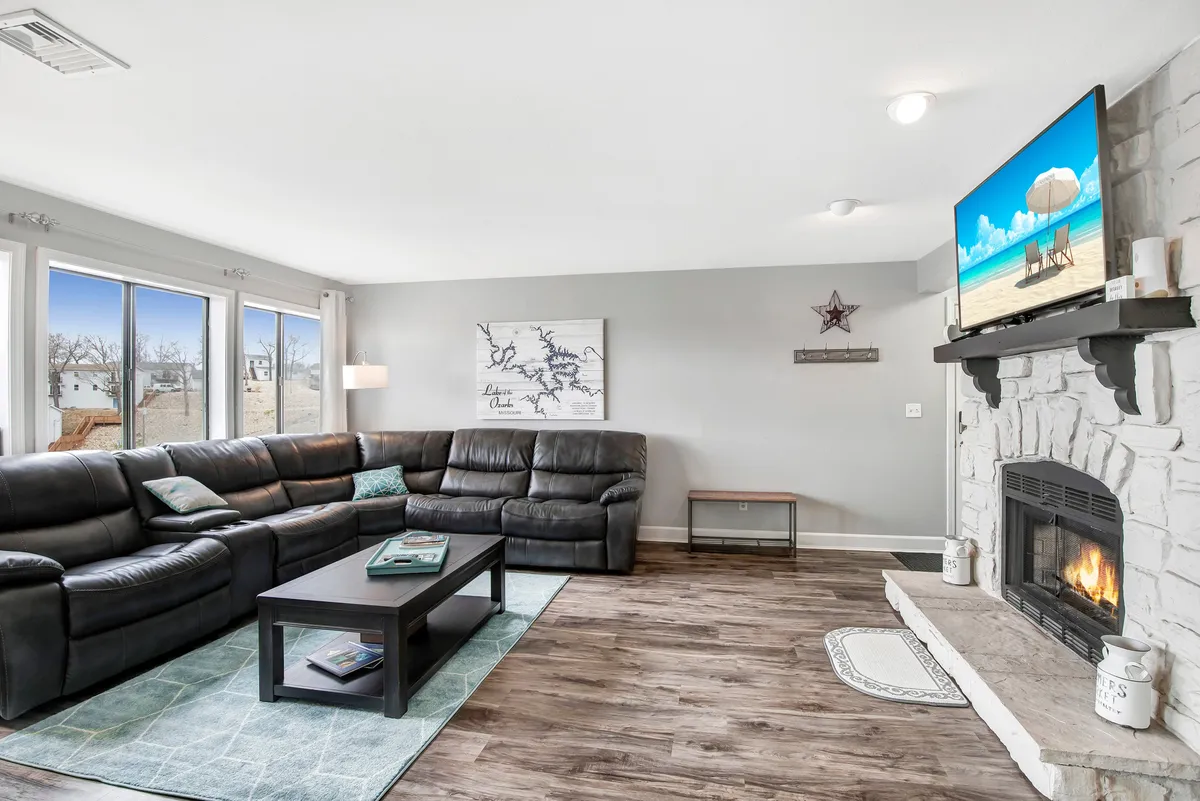 A spacious and comfortable living room featuring a large sectional sofa, a cozy fireplace, a flat-screen TV, and a coffee table. Large windows provide natural light and likely offer scenic views, suggesting a welcoming space ideal for group gatherings and relaxing after a day of activities.