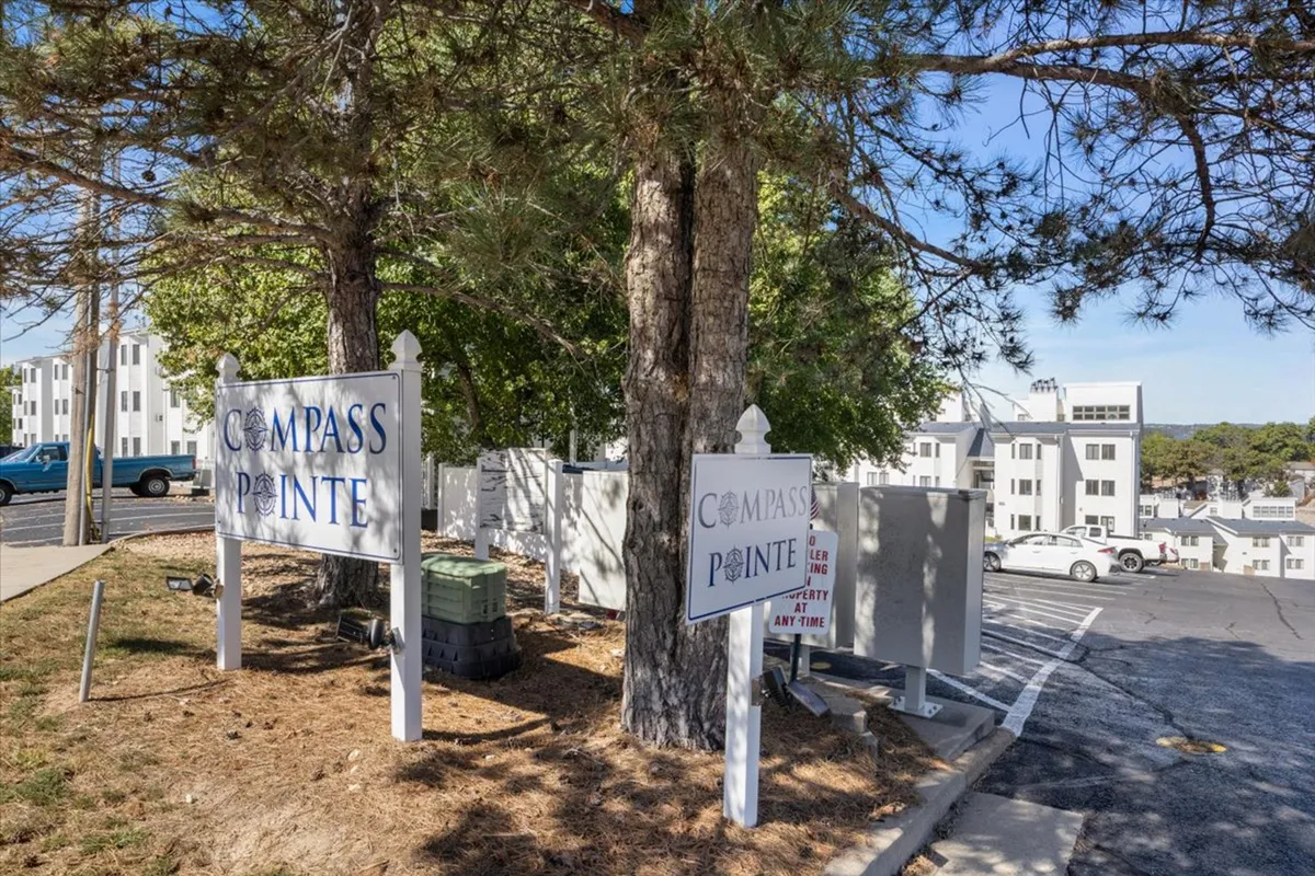 A welcoming entrance sign for Compass Pointe framed by tall trees and set against the backdrop of the property's buildings. The scene feels inviting and hints at a family-friendly community.