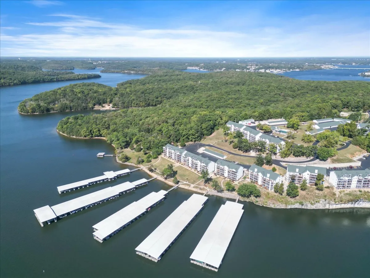 A wide view of marina docks stretching out over the calm lake, flanked by waterfront properties and lush greenery. The lake is the central focus, inviting the viewer to imagine boating, fishing, and paddleboarding right from the dock. The gentle evening light hints at sunset, with the water reflecting warm hues.