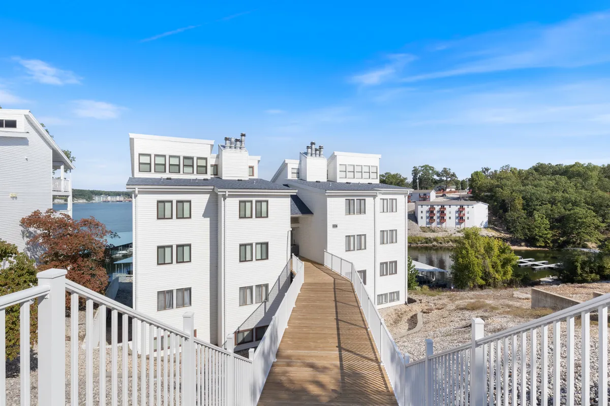 A lakeside walkway lined with trees, modern buildings in the background, and serene water views. The setting is peaceful, perfect for strolls, with sunset tones enhancing the inviting ambiance.