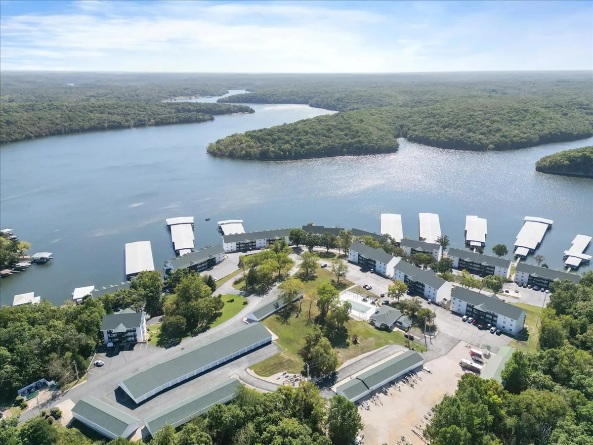 A tranquil lake scene with a dock stretching into the water, surrounded by greenery and distant buildings. The setting evokes the thrill of lakeside adventures, boating, and peaceful relaxation by the water.