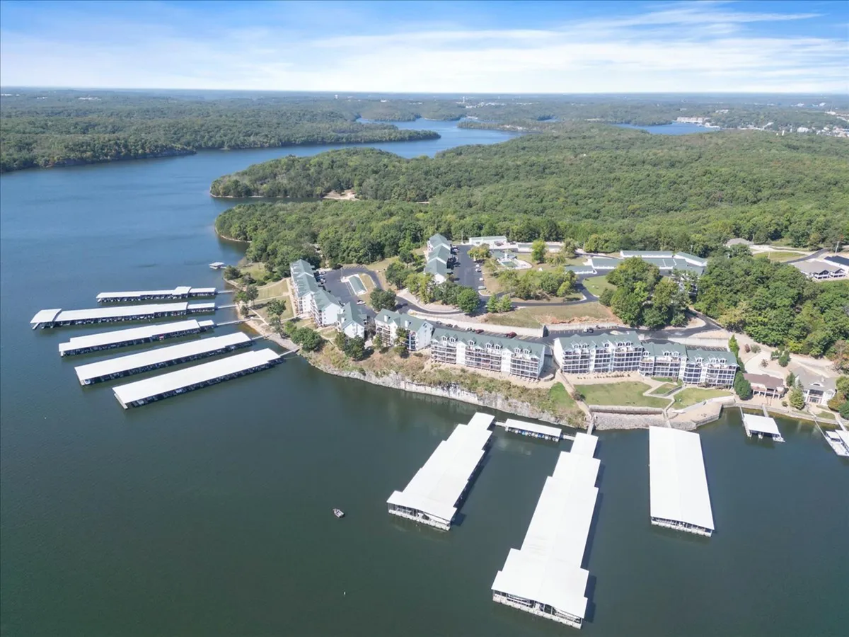 Scenic view of waterfront buildings, marinas, and lush green surroundings, with docks extending over the water. The setting is peaceful and showcases the natural beauty and outdoor opportunities of Osage Beach.