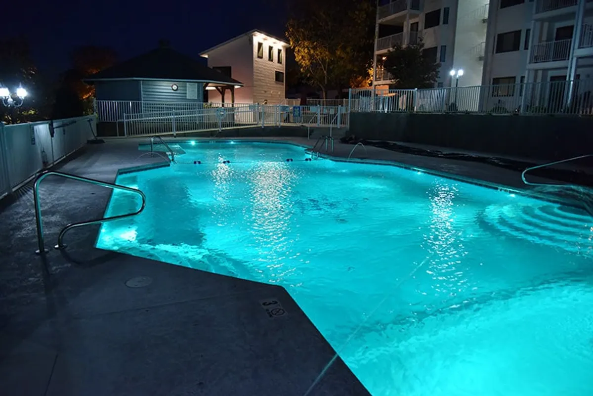 A beautifully illuminated pool at night, surrounded by a fence and low landscape lighting, creates a serene and magical atmosphere ideal for evening swims and social gatherings.