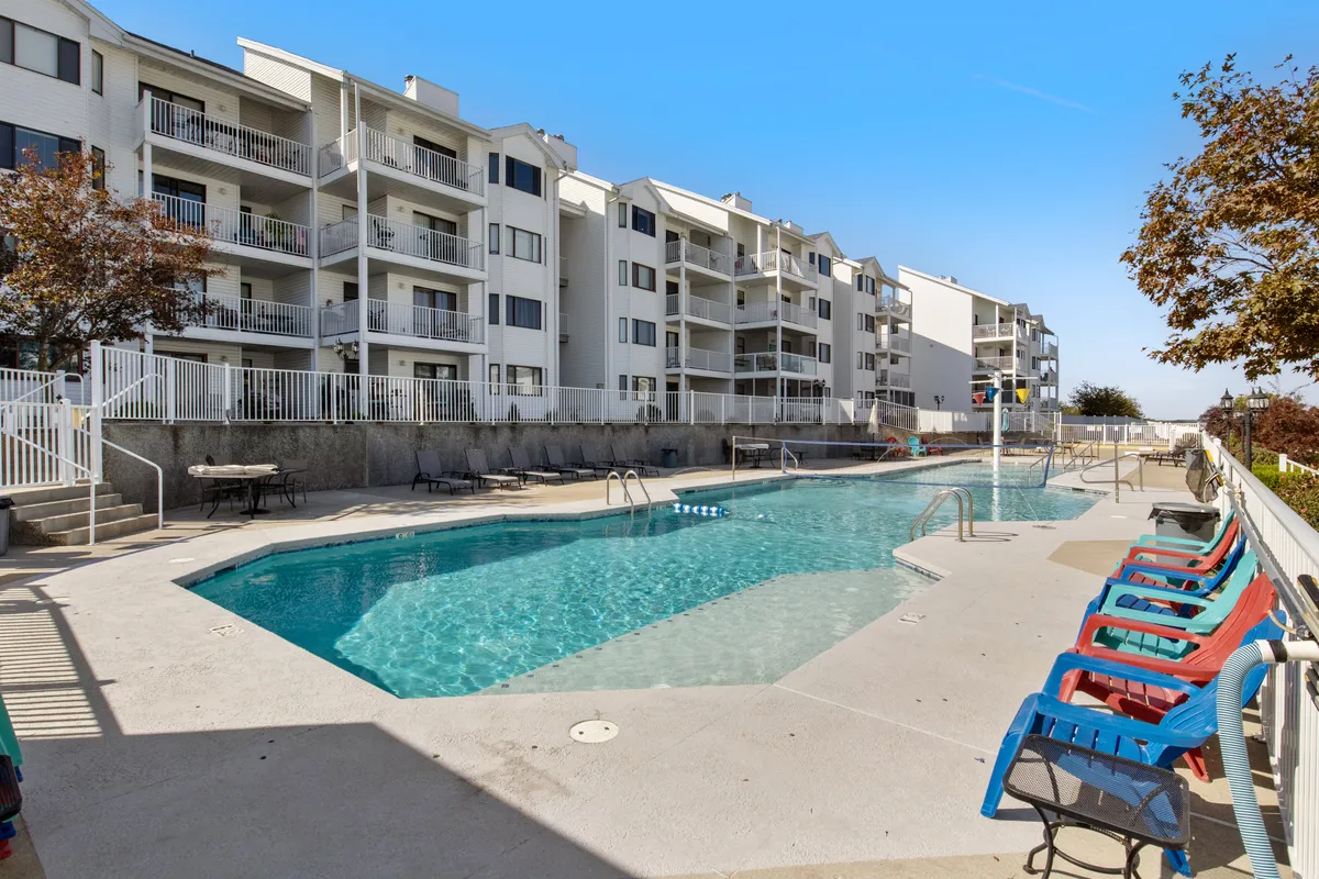 An inviting resort-style swimming pool surrounded by lounge chairs and apartment buildings. The pool area is designed for relaxation and socializing, with clear water and a tranquil atmosphere ideal for unwinding or group activities after golfing or exploring.